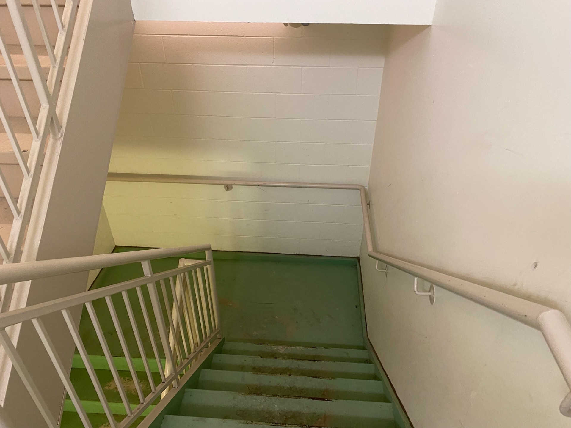 Condo stairwell before painting with discolored walls and green flooring